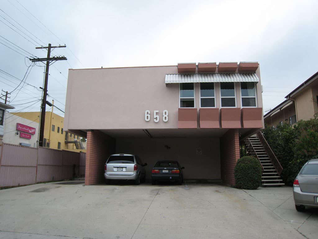 A West Hollywood dingbat apartment facade with decorative lettering and a carport below.